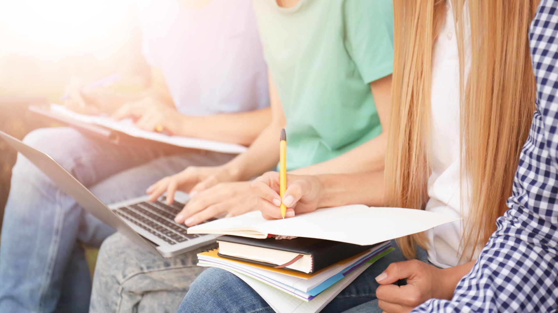 Gruppe von Menschen sitzend mit Laptop und Notizheft am Schoß, Köpfe der Personen sind nicht sichtbar