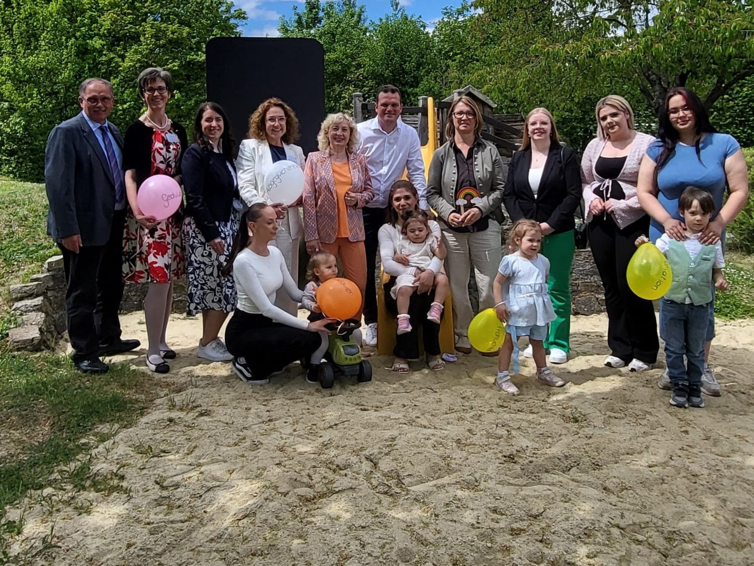 Gruppenfoto von Erwachsenen und Kindern im Freien, einige halten bunte Luftballons.