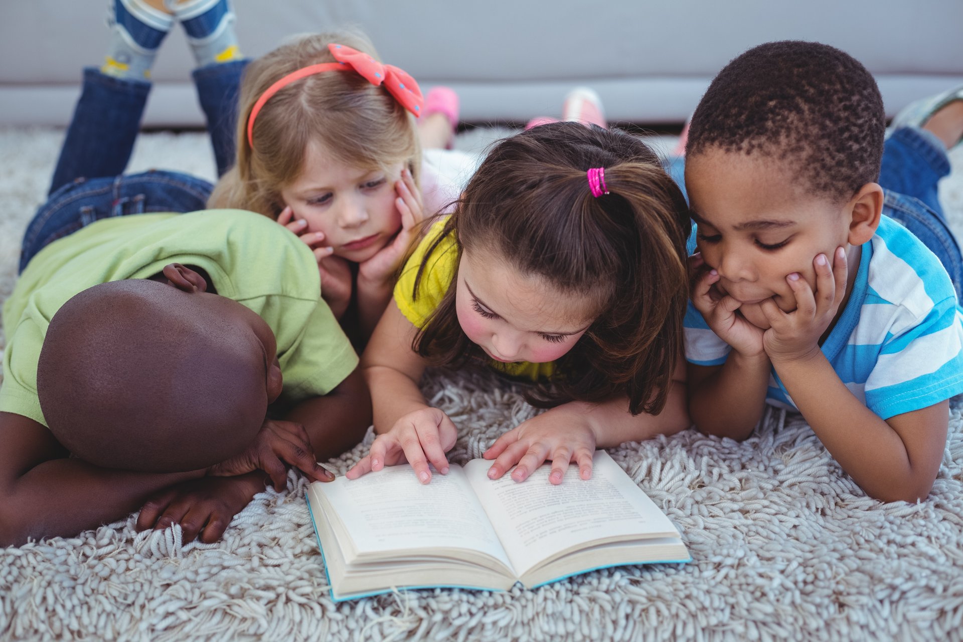 vier Kinder unterschiedlicher Hautfarbe liegen auf dem Boden und lesen ein Buch miteinander