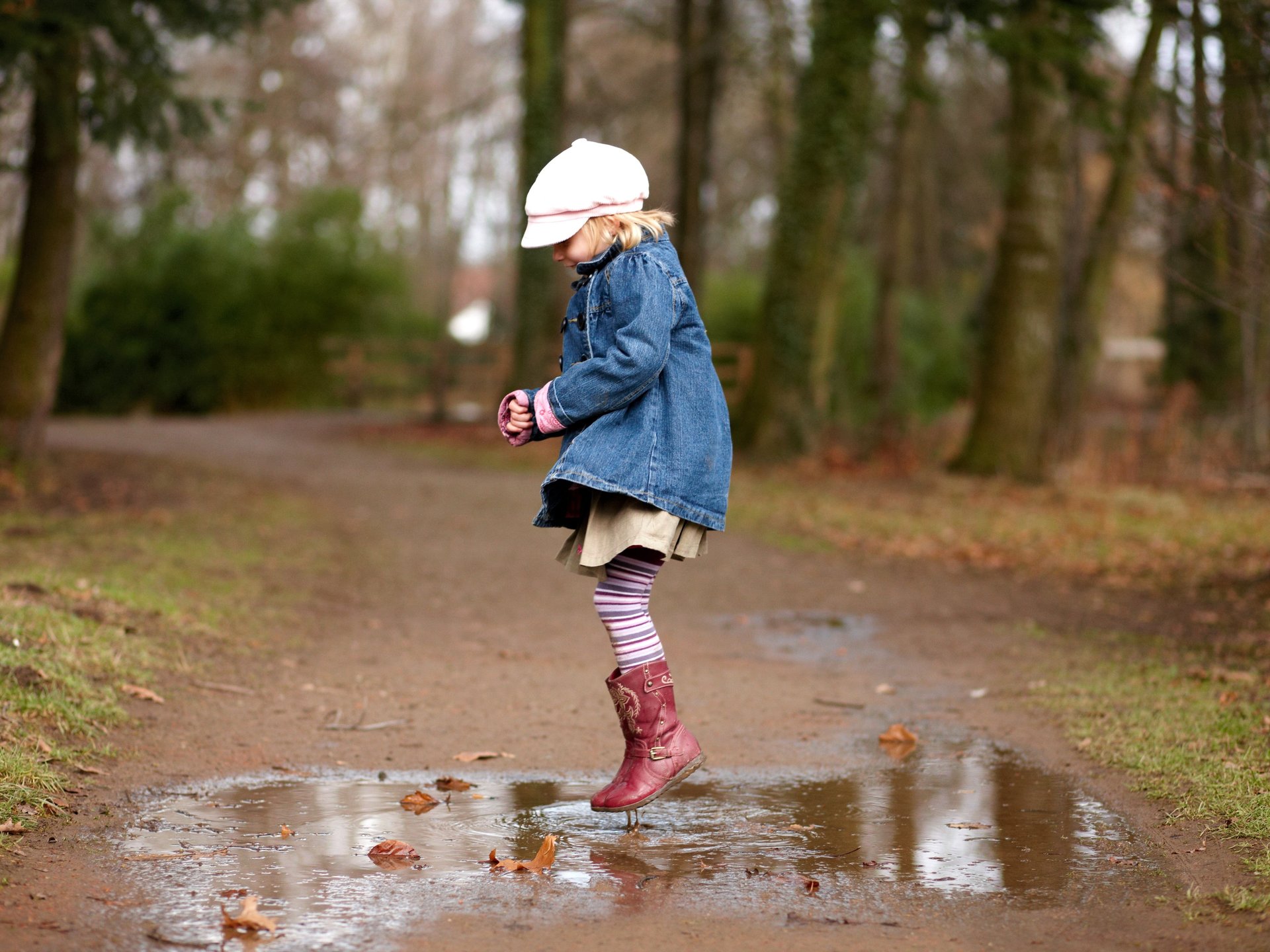 Kind spielt und springt in eine Pfütze auf einem Weg im Freien.