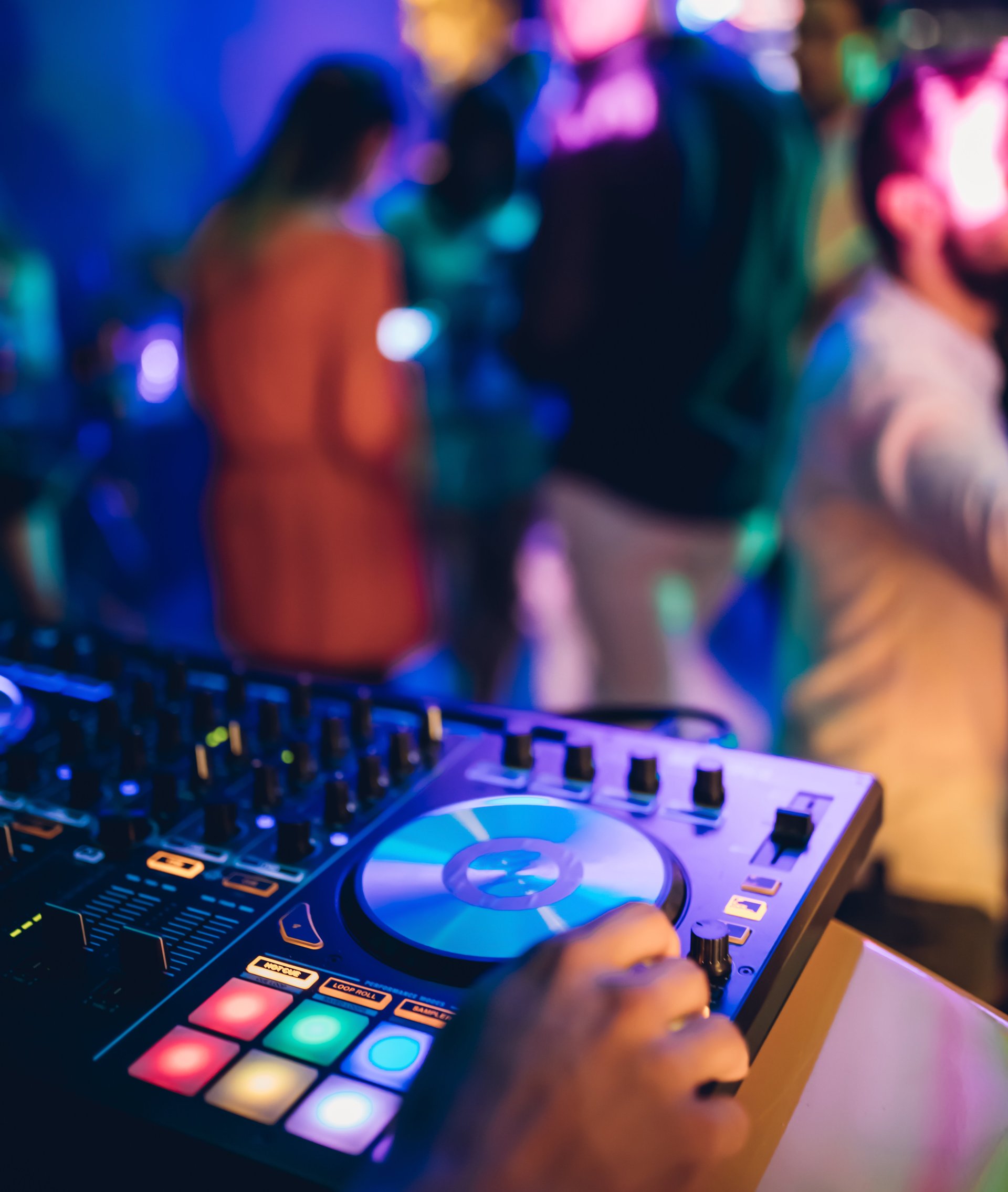 DJ legt in der Disco auf; im Hintergrund tanzende junge Menschen